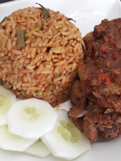 A picture of Jollof rice with fried chicken and cucumber.