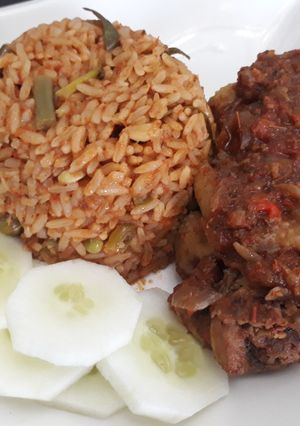 A picture of Jollof rice with fried chicken and cucumber.