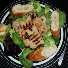A picture of Grilled pork with salad and garlic bread.