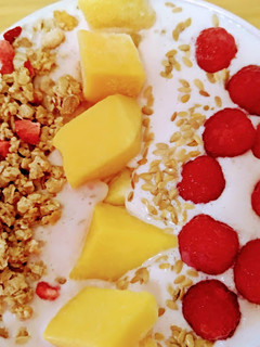 Una foto de Cuenco de yogur con frambuesas, mango, granola con fresas y semillas de sésamo