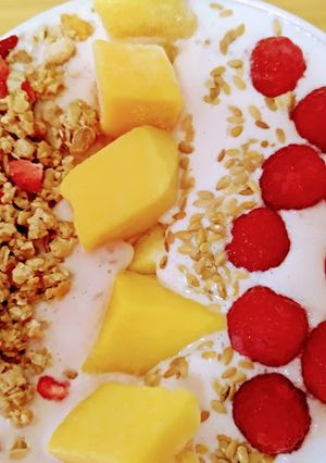 Una foto de Cuenco de yogur con frambuesas, mango, granola con fresas y semillas de sésamo