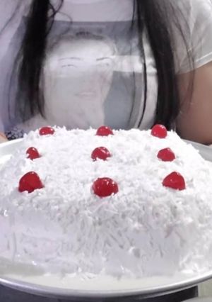 Una foto de Pastel de Tres leches cubierto de Crema y Coco rallado con cerezas
