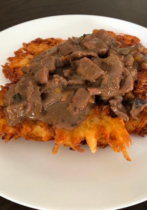 A picture of Beef goulash with mushrooms served on potato pancakes.
