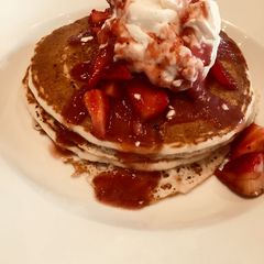 A picture of Pancakes loaded with whipped cream and strawberries.