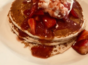 A picture of Pancakes loaded with whipped cream and strawberries.