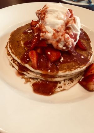 A picture of Pancakes loaded with whipped cream and strawberries.