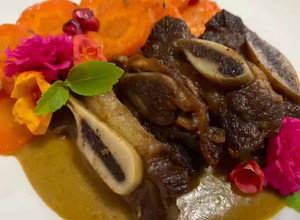 Una foto de Costillas de res confitadas acompañadas de una salsa de guaje con vino rosado