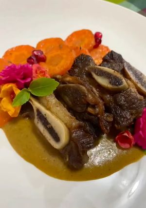 Una foto de Costillas de res confitadas acompañadas de una salsa de guaje con vino rosado