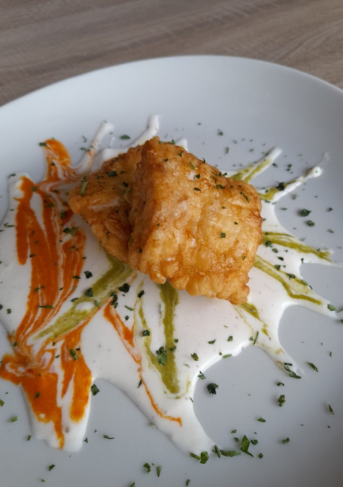 Una foto de Suprema de merluza frita en lecho de crema de pimientos