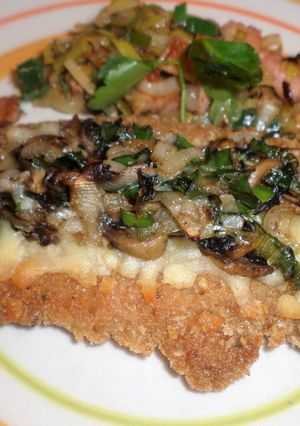 Una foto de Milanesa de cerdo con cobertura de hongo y parmesano y guarnición de panceta y puerro