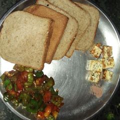 A picture of Stir fry capsicum and tomatoes with paneer cube and brown bread.