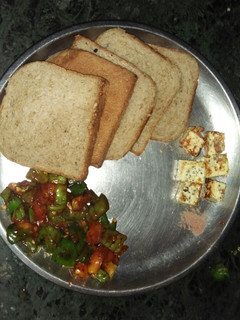 A picture of Stir fry capsicum and tomatoes with paneer cube and brown bread.