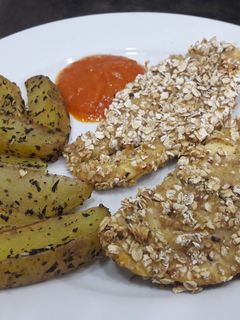 Una foto de Pollo con crujiente de avena y patatas gajo especiadas al horno