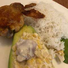 A picture of Pollo frito con arroz y palta rellena de pollo y choclo dulce.