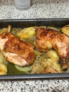 Una foto de Muslos de pollo al horno con una cama de papas y cebolla