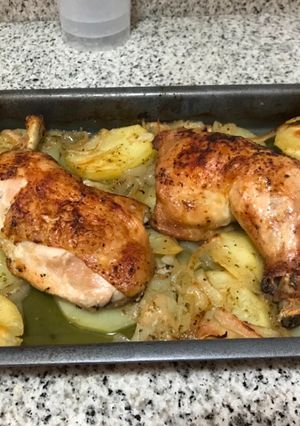 Una foto de Muslos de pollo al horno con una cama de papas y cebolla