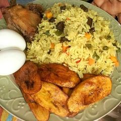 A picture of Fried rice with fried plantain,boiled egg and chicken.