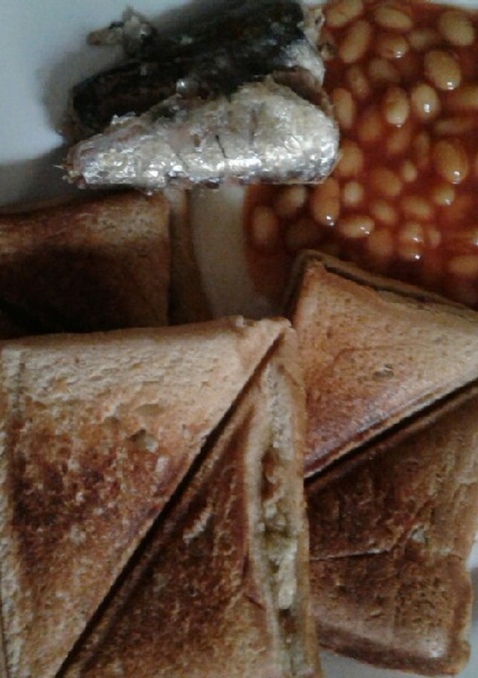 A picture of Scrambled eggs in a Toast with sardine and baked beans.
