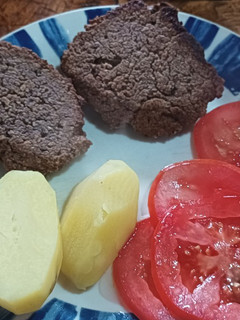 Una foto de Hamburguesa de porotos negros con papas cocidas y ensalada de tomate