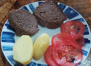 Una foto de Hamburguesa de porotos negros con papas cocidas y ensalada de tomate