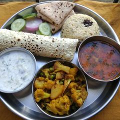 A picture of Lunch platter sabji dal raita rice papad roti salad.