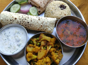 A picture of Lunch platter sabji dal raita rice papad roti salad.