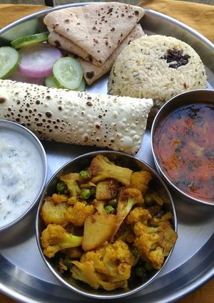 A picture of Lunch platter sabji dal raita rice papad roti salad.