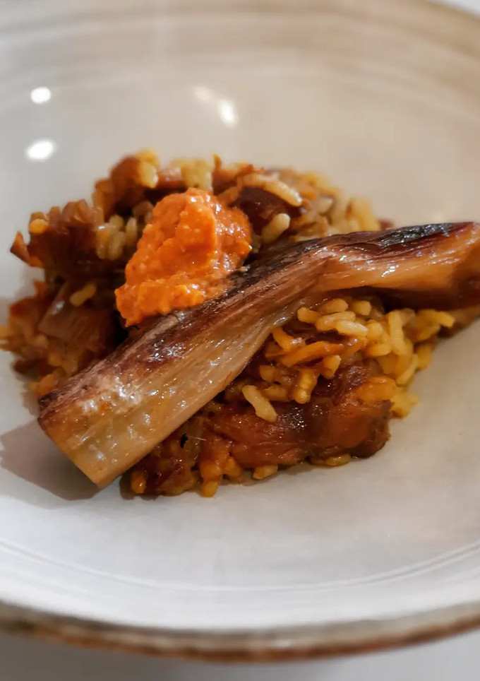 Una foto de Arroz de calçots, alcachofas y carrilleras con romesco