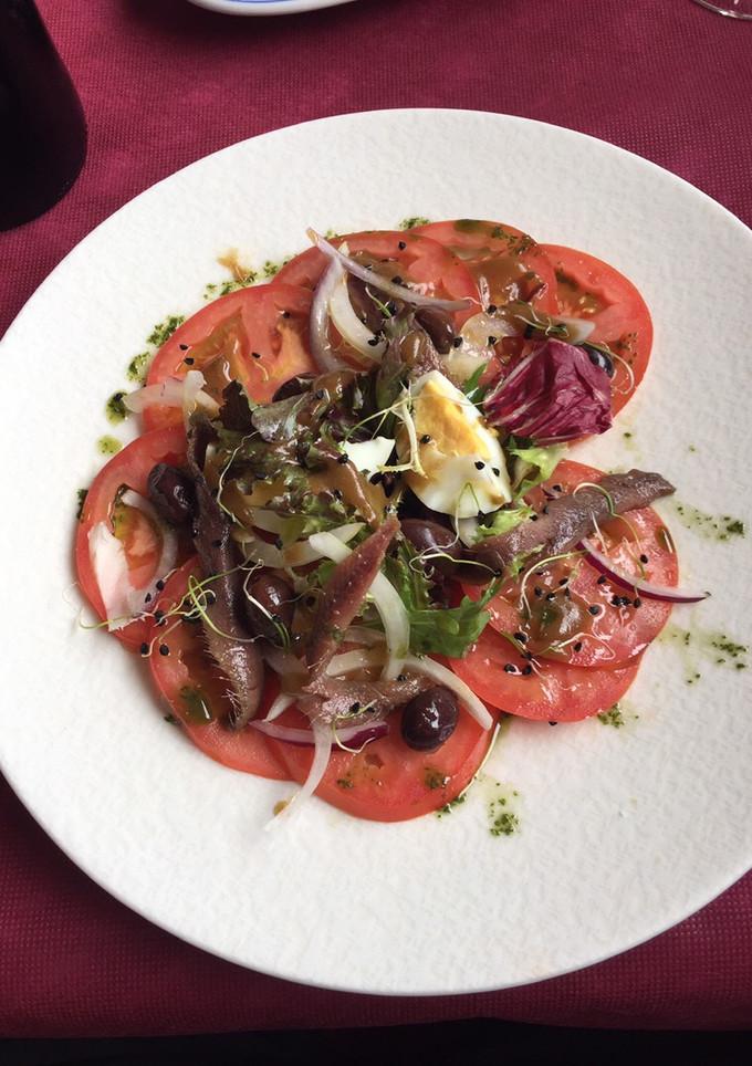 Una foto de Ensalada de tomate con anchoas en salazón, huevo, cebolla y brotes con vinagreta de naranja