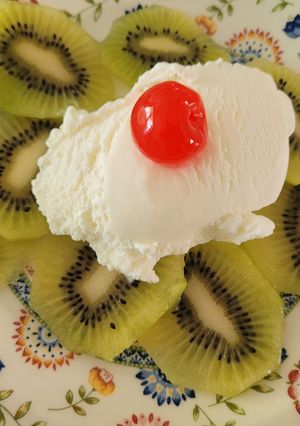 Una foto de Kiwis con helado de leche merengada y guindas en almíbar