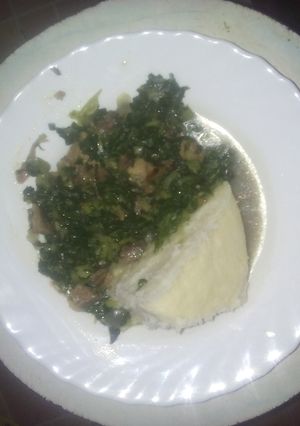 A picture of Ugali served with fried spinach  mixed with beef meat.