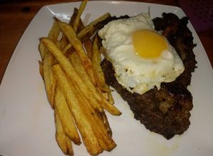 Una foto de Bife de chorizo al ajillo a caballo con papas bravas