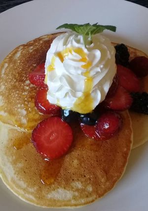 A picture of Pancakes with whipped cream and berries.