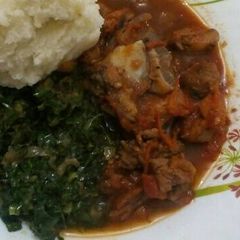 A picture of Fried Goat meat served with greens and ugali.