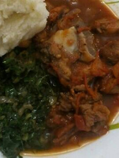 A picture of Fried Goat meat served with greens and ugali.