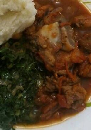 A picture of Fried Goat meat served with greens and ugali.