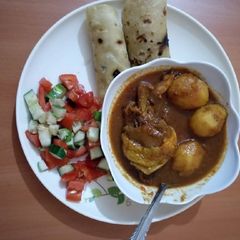 A picture of Chicken potato stew with chapati and tomato cucumber salad.