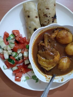 A picture of Chicken potato stew with chapati and tomato cucumber salad.