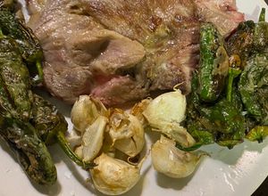 Una foto de Chuletas de aguja con ajos enteros y pimientos de Padrón semipicantes