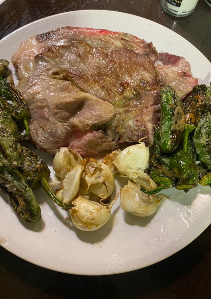 Una foto de Chuletas de aguja con ajos enteros y pimientos de Padrón semipicantes