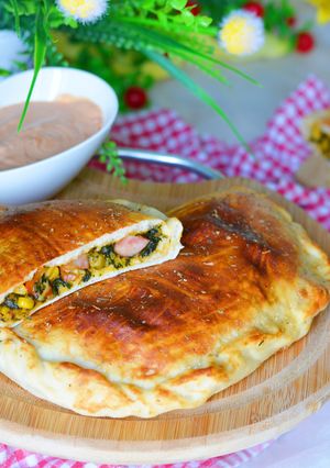 Zdjęcie przepisu Calzone z kiełbasą w towarzystwie szpinaku i kolorowych warzyw.