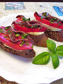 Una foto de Anchoas, tomates cornudo de Andes y mozzarella sobre rebana de baguette de semillas - tapas