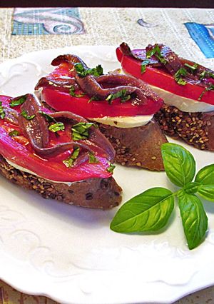 Una foto de Anchoas, tomates cornudo de Andes y mozzarella sobre rebana de baguette de semillas - tapas