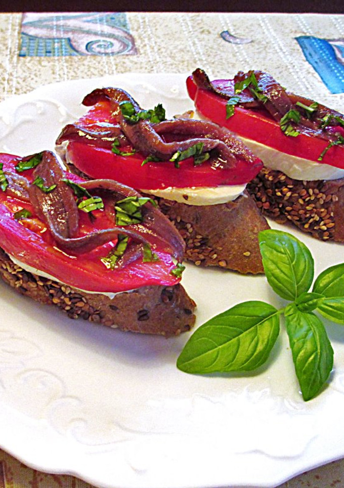 Una foto de Anchoas, tomates cornudo de Andes y mozzarella sobre rebana de baguette de semillas - tapas