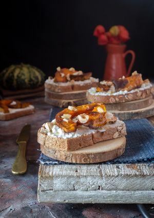 A picture of DARK MULTIGRAIN BREAD CROSTINI WITH GOAT RICOTTA, ROASTED SQUASH, AND HONEY.