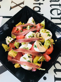 Una foto de Ensalada de tomate, mozzarella, aguacate y anchoas, con albahaca fresca y regada con Aceite oliva