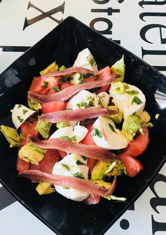 Una foto de Ensalada de tomate, mozzarella, aguacate y anchoas, con albahaca fresca y regada con Aceite oliva
