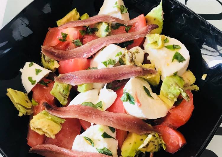 Ensalada de tomate, mozzarella, aguacate y anchoas, con albahaca fresca y regada con Aceite oliva