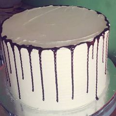 A picture of Rainbow cake decorated with butter cream and chocolate drips.
