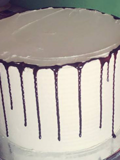 A picture of Rainbow cake decorated with butter cream and chocolate drips.